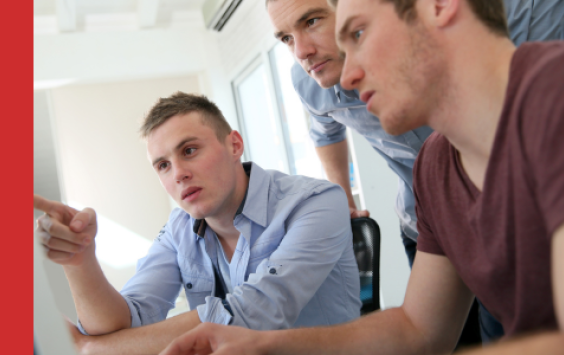 Three young male work colleagues looking at computer screen during training session